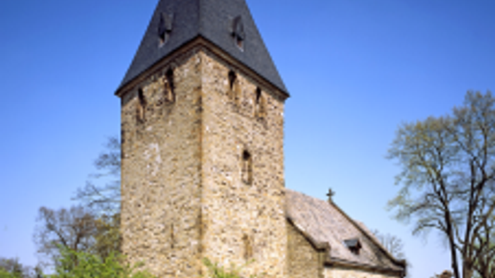 Historische Steinkirche mit hohem Glockenturm vor klarem blauem Himmel.