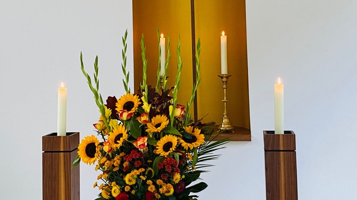 Eleganter Altar mit lebhaften Blumen, Kerzen und einem goldenen Kreuz hinter einem erleuchteten Fenster.