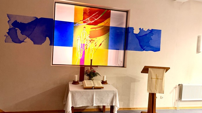Religiöser Altarraum mit lebendigem Wandgemälde, Kerzen, Büchern und einem Lesepult in einer ruhigen Innenraumatmosphäre.