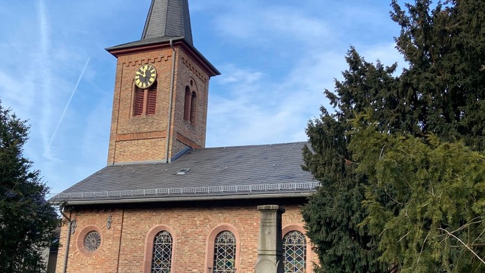 Bild der Nazarethkirche in Frankfurt Eckenheim von Süden her. Die Kirche hat einen spitzen Turm mit einem Kreuz . Das Dach ist mit Schiefer gedeckt. Die Wände bestehen aus gelben und roten Klinker-Steinen. In den Wänden sind große farbige Fenster mit Blei