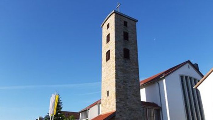Moderne Kirche mit hohem Steinglockenturm und rotem Ziegeldach unter klarem blauem Himmel.