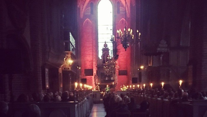 En højtidelig kirkelig gudstjeneste med et lysoplyst alter og en samlet menighed i en svagt oplyst, storslået katedral.