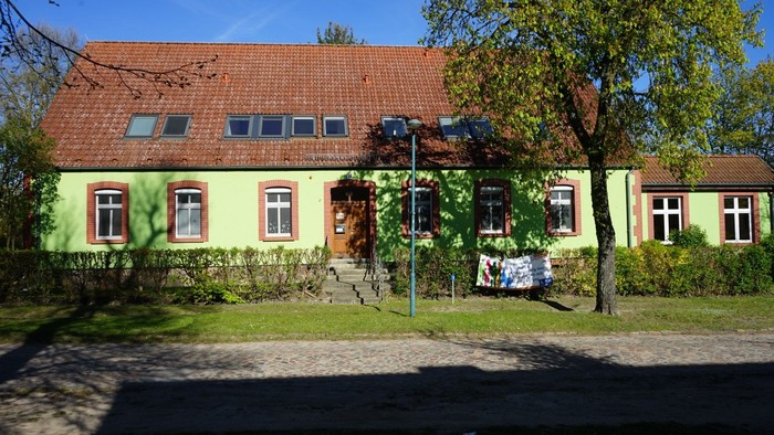 Langgestrecktes Gemeindehaus mit grüner Fassade, roten Fensterrahmen und braunem Satteldach.