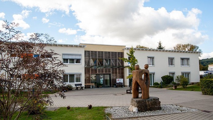 Modernes Gebäude mit Skulptur im Vordergrund, gepflegtem Garten und klarem Himmel