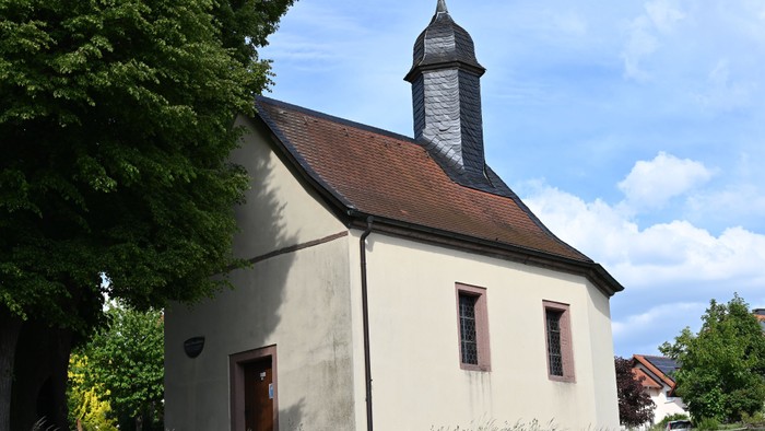 Kleine weiße Kirche mit steilem Dach, Glockenturm und umgeben von Grün unter blauem Himmel.