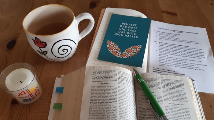 Gemütlicher Lernplatz mit Buch, Lesezeichen, Kaffee, Kerze und einem motivierenden Buch neben den aufgeschlagenen Seiten.