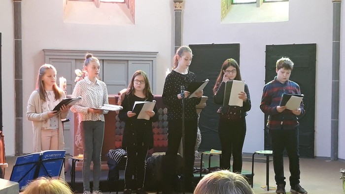 Eine Gruppe junger Sänger, die in einer Kirche mit Notenblättern in der Hand Musik aufführt.