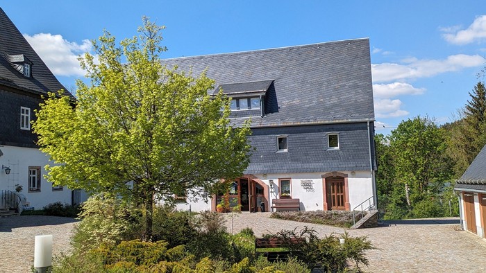 Haus mit schwarzem Dach und grünem Baum davor
