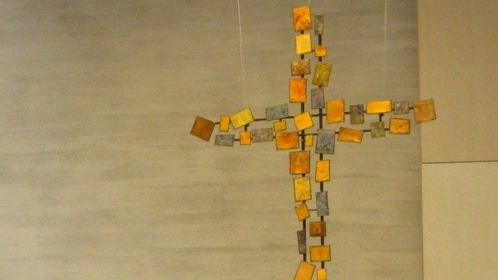 Eine kreuzförmige Skulptur aus verschiedenen farbigen Blöcken hängt an einer Wand.