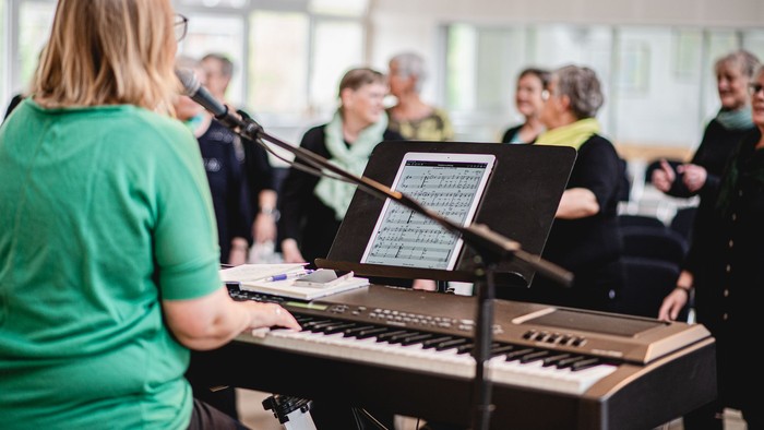 En kvinde spiller keyboard mens en kor sanges i lys rum