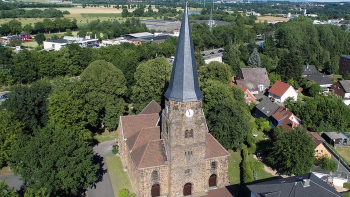 Luftaufnahme einer historischen Kirche, umgeben von üppigem Grün und einem malerischen Dorf.