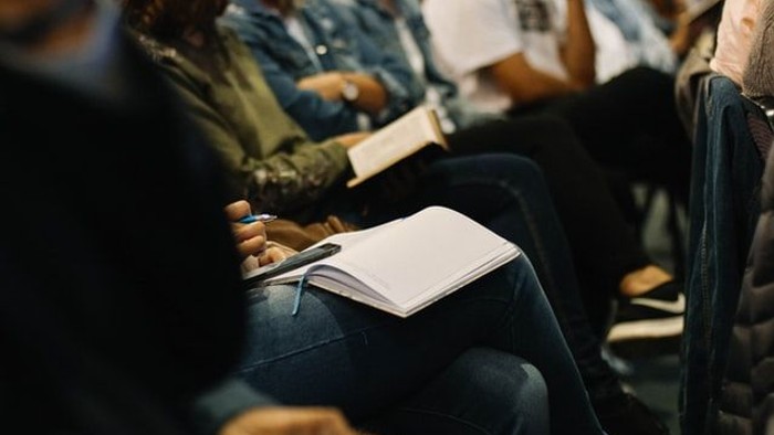 Person sitzt mit aufgeschlagenem Buch auf Stuhl in Menschenmenge