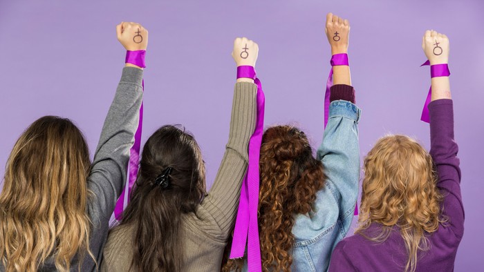 Vier Mädchen mit erhobenen Armen und pinken Armbändern vor lila Hintergrund