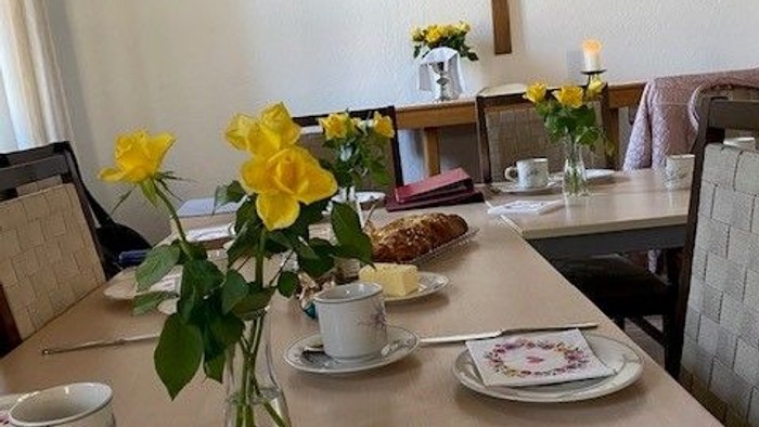Elegante Tischdekoration mit Blumenarrangements, Tassen, Tellern und einem Kreuz in einem ruhigen Raum.