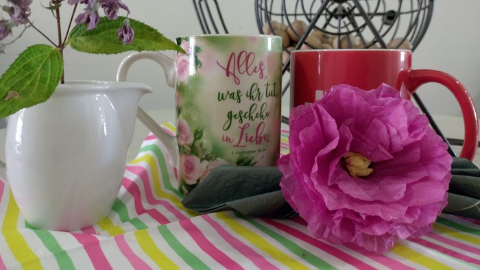 Bunte Tischdekoration mit Blumenbechern, Krug, gestreiftem Tuch, frischen Blumen und einem dekorativen Fächer.