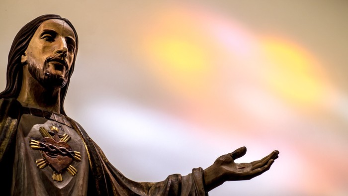 Die Statue eines Mannes mit Herz und ausgestreckter Hand vor einem hellen Hintergrund.