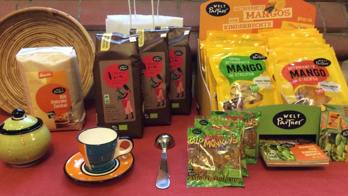 Verschiedene Fair-Trade-Tees, Kaffee und Snacks, arrangiert auf einem roten Tischtuch mit einem Kaffeeservice.