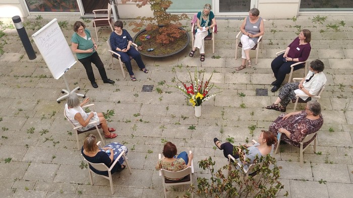 Eine Gruppe von Menschen sitzt im Freien auf Stühlen und genießt eine Veranstaltung.