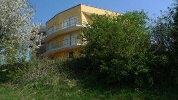 Modernes gelbes Wohngebäude, umgeben von üppigem Grün und Bäumen an einem sonnigen Tag.