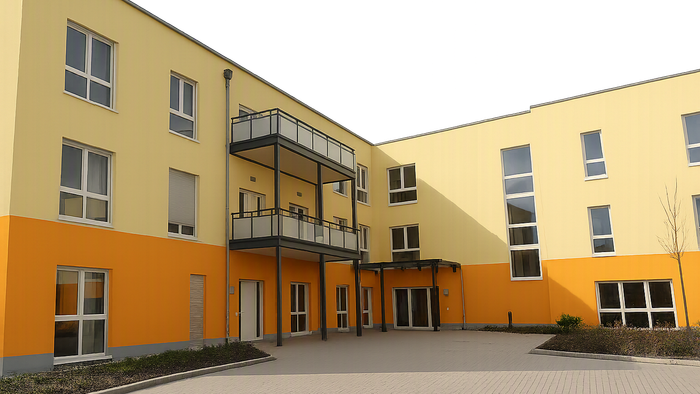 Modernes Wohngebäude mit hellgelben und orangefarbenen Akzenten, das Balkone und einen zentralen Innenhof-Eingang aufweist.