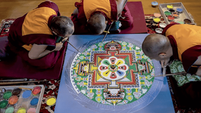 Trois moines créent un mandala coloré sur une table.