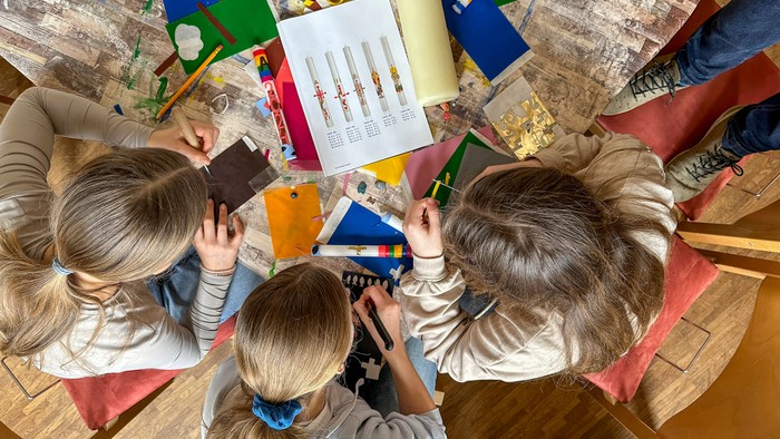 Drei Kinder arbeiten gemeinsam an einem Bastelprojekt an einem Tisch, umgeben von verschiedenen Materialien.
