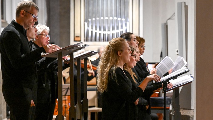 Ein Chor tritt in einer prächtigen Kirche mit einer Orgelkulisse auf und singt nach Notenblättern.