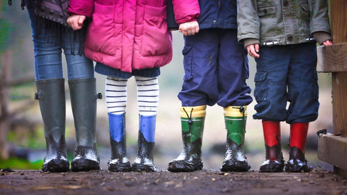 Eine Gruppe von Kindern in bunten Gummistiefeln und Outdoor-Kleidung steht gemeinsam draußen.