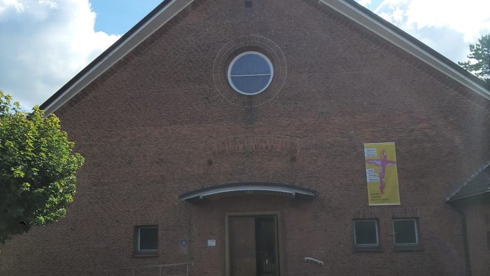 Moderne Backsteinkirche mit zentralem Rundfenster, kleinem Kirchturm und gepflastertem Hofeingang.