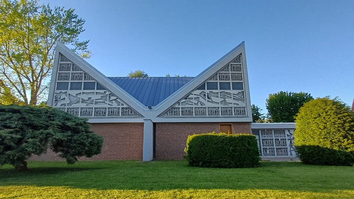 Moderne Kirche hinter einer Wiese, umgeben von Bäumen.