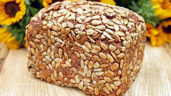 Vollkornbrot mit Haferflocken, umgeben von leuchtend gelben Blumen.