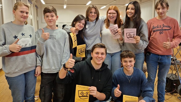 Eine fröhliche Gruppe von Schüler:innen, die Zertifikate halten und in einem Klassenzimmer Daumen hoch zeigen.