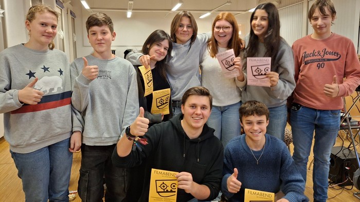 Eine fröhliche Gruppe von Schüler:innen, die Zertifikate halten und in einem Klassenzimmer Daumen hoch zeigen.