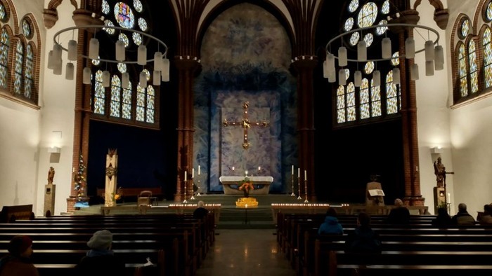Innenraum einer Kirche mit Altarraum, Kirchenbänken und farbenfrohen Fenstern