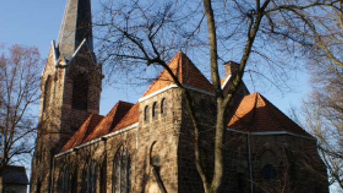 Historische Kirche mit hohem Turm und rotem Ziegeldach vor klarem blauem Himmel.