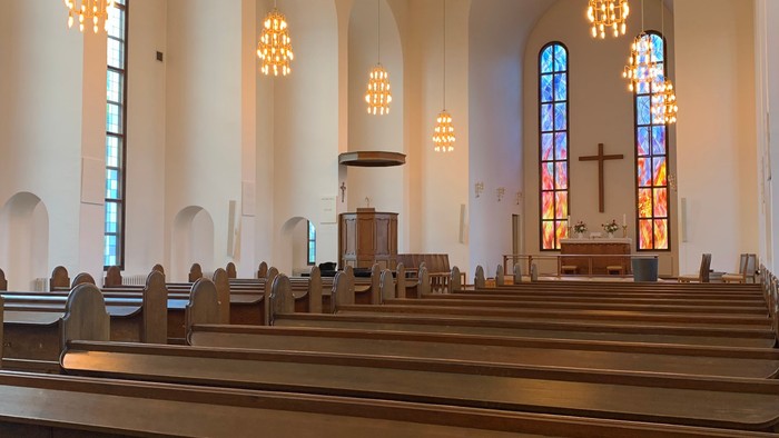 Indre del af en stor, lys kirke med høje buegange og lysende lys.
