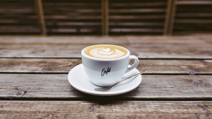 En lille café i en white kop på en plate med en lille skøb på et træbord