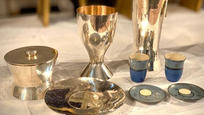 Elegante silberne sakrale Gefäße, darunter ein Kelch, ein Weihrauchfass und zeremonielle Platten, auf einem Tisch.