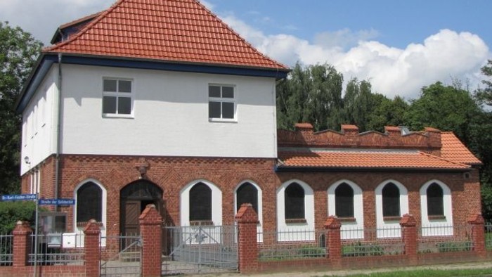 Weißes Gebäude mit rotem Dach und Turm, umgeben von einem Zaun