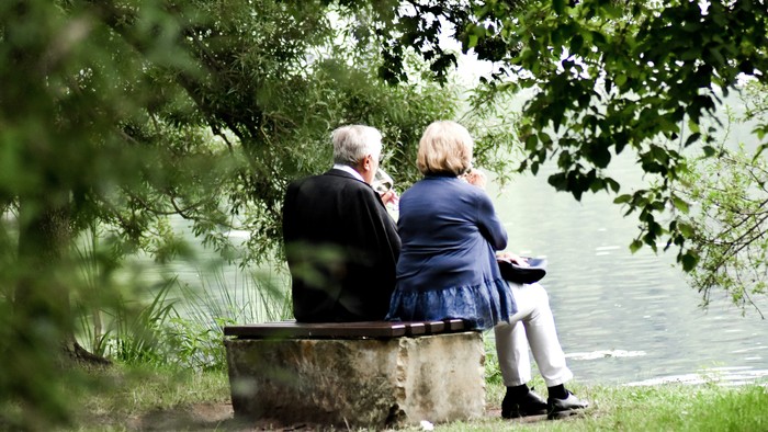 Ein älteres Paar sitzt auf einer Bank am Wasser und schaut in die Ferne.