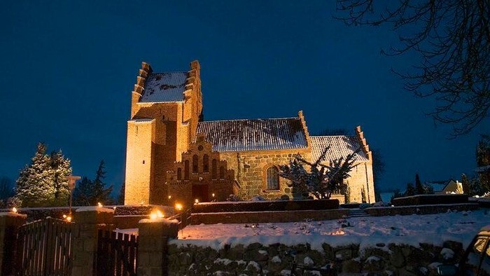 Sneklædt kirke oplyst om natten med en mørk himmel.