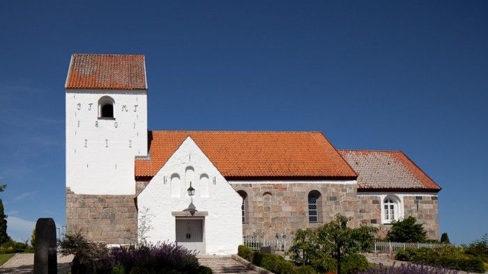 En hvid kirke med røde tag og tårn foran en klar blå himmel