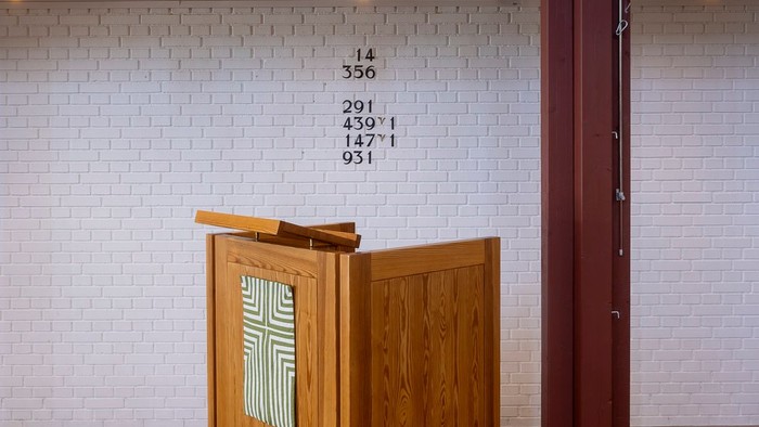 En træpult i kirke med korset på forside og en liste med tal på bagside