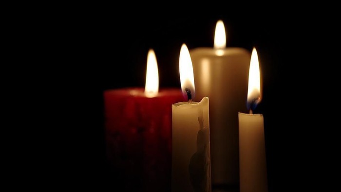 Tre tændte stearinlys med flammer, der gløder mod en mørk baggrund, og skaber en varm og rolig stemning.