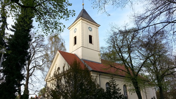 Weiße Kirche mit Uhrturm und rotem Dach zwischen Bäumen
