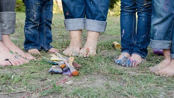 Bunte Farben auf den nackten Füßen von Kindern, die auf grasigem Boden stehen.