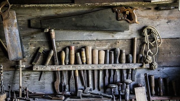 Eine rustikale Sammlung von alten Handwerkzeugen und Sägen, angebracht an verwitterten Holzregalen.