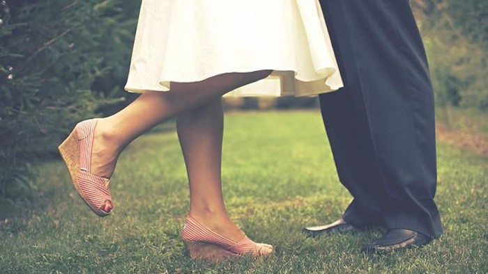 Paar, das im Freien in Hochzeitskleidung auf einem üppigen grünen Rasen spaziert.