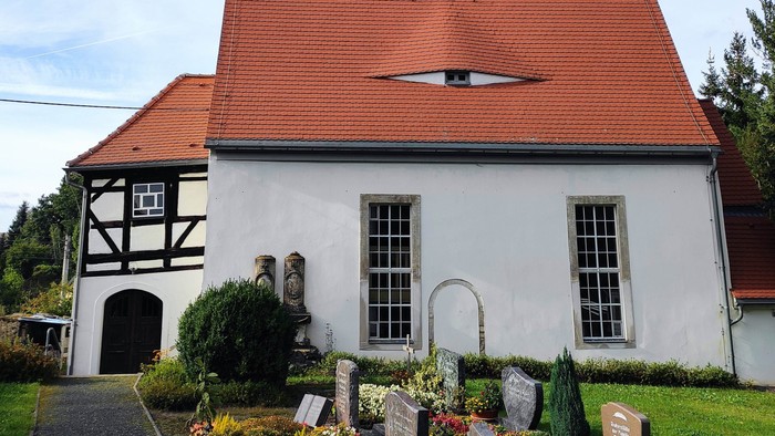 Kirchengebäude mit rotem Dach und hohem Turm mit Uhr und Wetterfahne