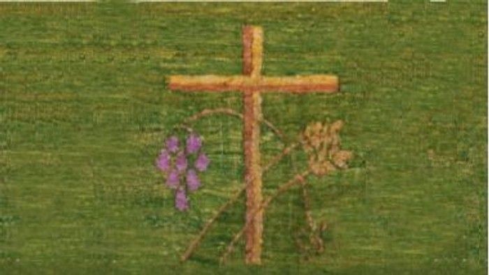 Ein hölzernes Kreuz auf einem grasbewachsenen Feld mit violetten Blumen und getrockneten Pflanzen in der Nähe.